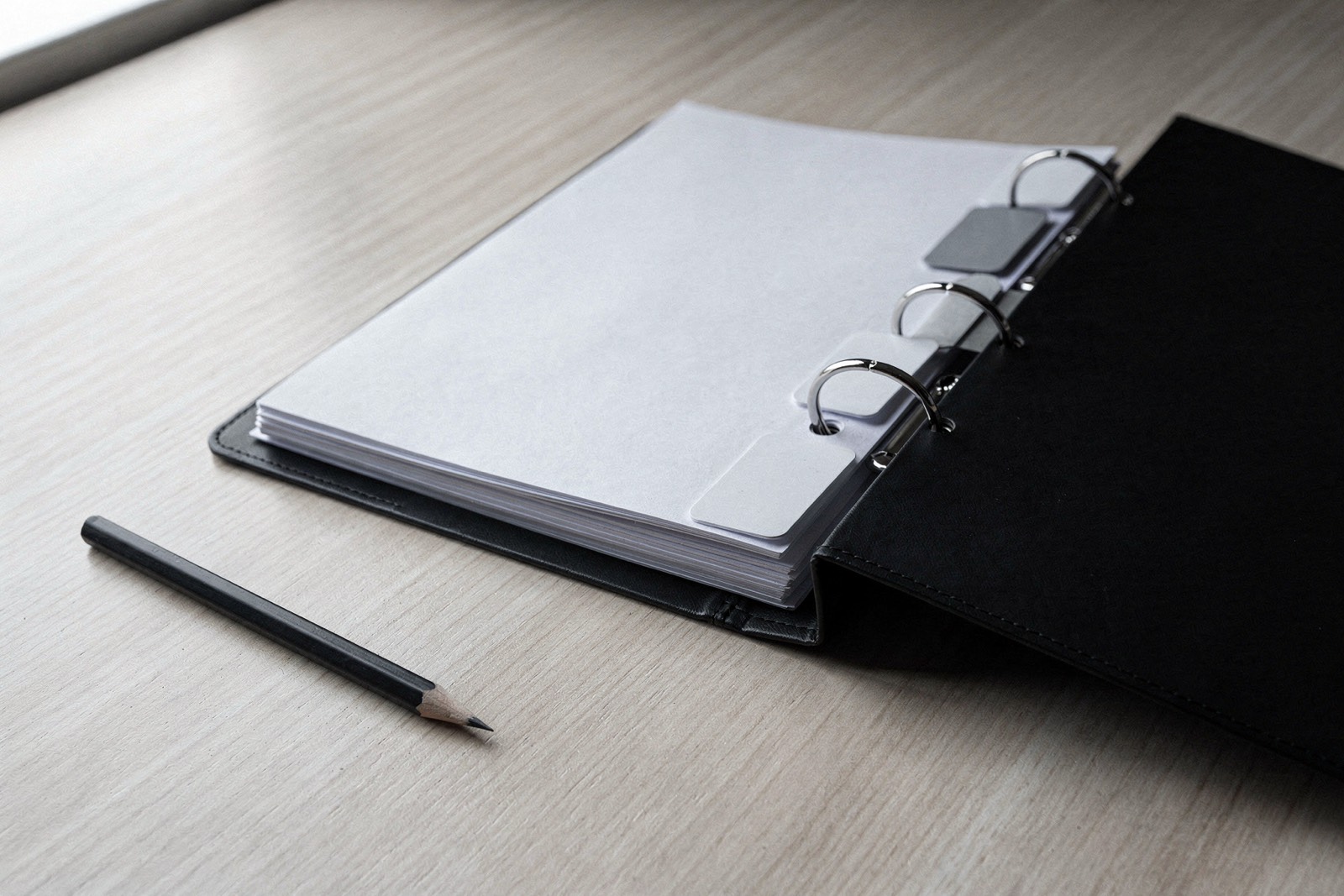 An open black ring binder with blank index dividers on a wooden table